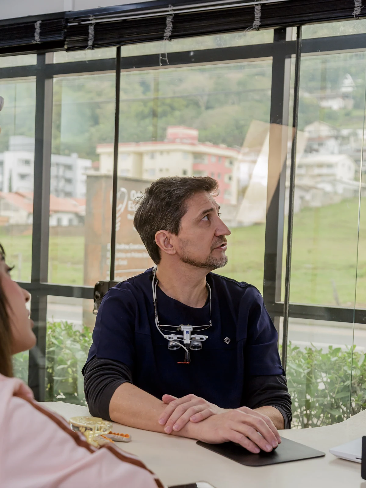 Dr. Rafael Luis Pamplona em consulta, com lupas de aumento, na sala de atendimento da clínica